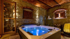 A stone-walled room with a hot tub, wooden cabinets, and a glass door.