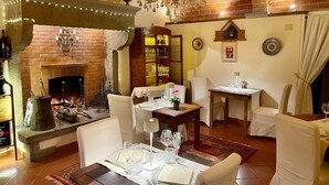 A dining area with a brick fireplace, chandelier, and a table set for four. - Cascina Borgo Dolci Colline-Limonaia in Castiglion Fiorentino (Castiglion Fiorentino)