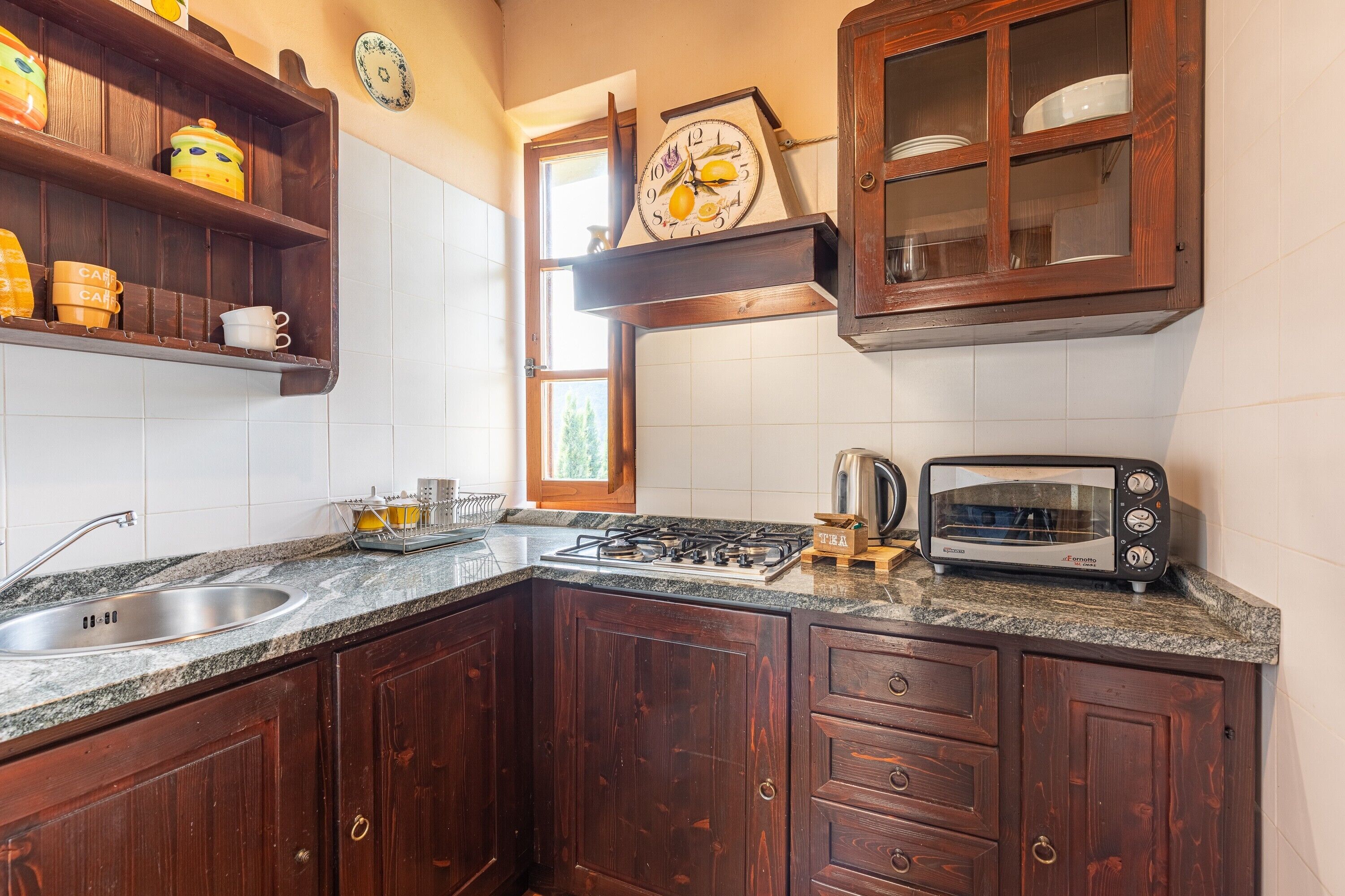 Una cucina con mobili in legno, un piano di lavoro in granito, forno integrato, un tostapane e una sveglia appesa al muro.