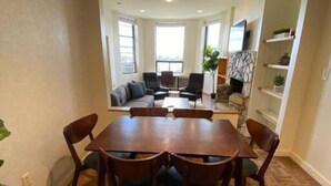 A dining area with a large wooden table and chairs, surrounded by a herringbone-patterned wooden floor. - Wonderful Fenway 3br/2ba | Steps from Fenway Park! (Boston)
