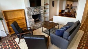 A living room with a stone fireplace, a television mounted above it, a sofa, a coffee table, and a patterned rug. - Wonderful Fenway 3br/2ba | Steps from Fenway Park! (Boston)