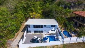 Uma casa moderna de dois andares com piscina, um pátio com espreguiçadeiras e um quintal cercado.