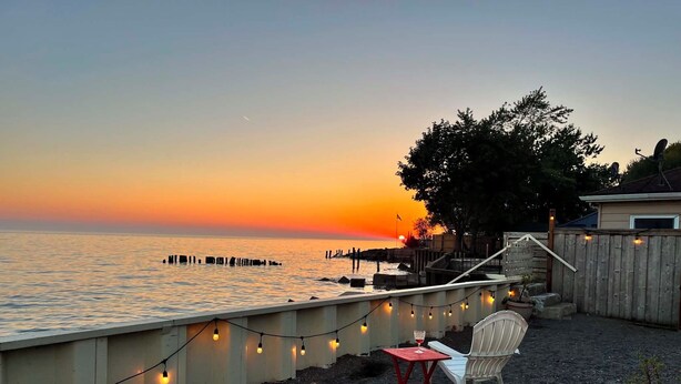 A waterfront patio with a view of the sunset, a wooden deck, and a chair.
