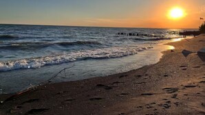 A beach with the sun setting over the ocean, waves gently crashing onto the shore, and a few people walking along the beach.