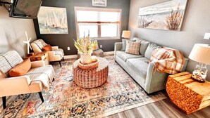 A cozy living room with a sofa, armchairs, a coffee table, and a TV mounted on the wall.