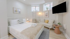 Een moderne slaapkamer met een groot bed, een bank, een kleine tafel en een aan de muur bevestigde televisie.