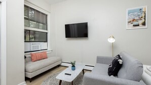 A modern living room with a grey sofa, a small coffee table with a plant, a mounted TV, and a framed picture on the wall. - Centrally Located Basic Studio (Boston)