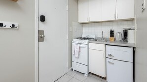 A compact kitchen with white cabinets, a stove, and a sink. - Centrally Located Basic Studio (Boston)
