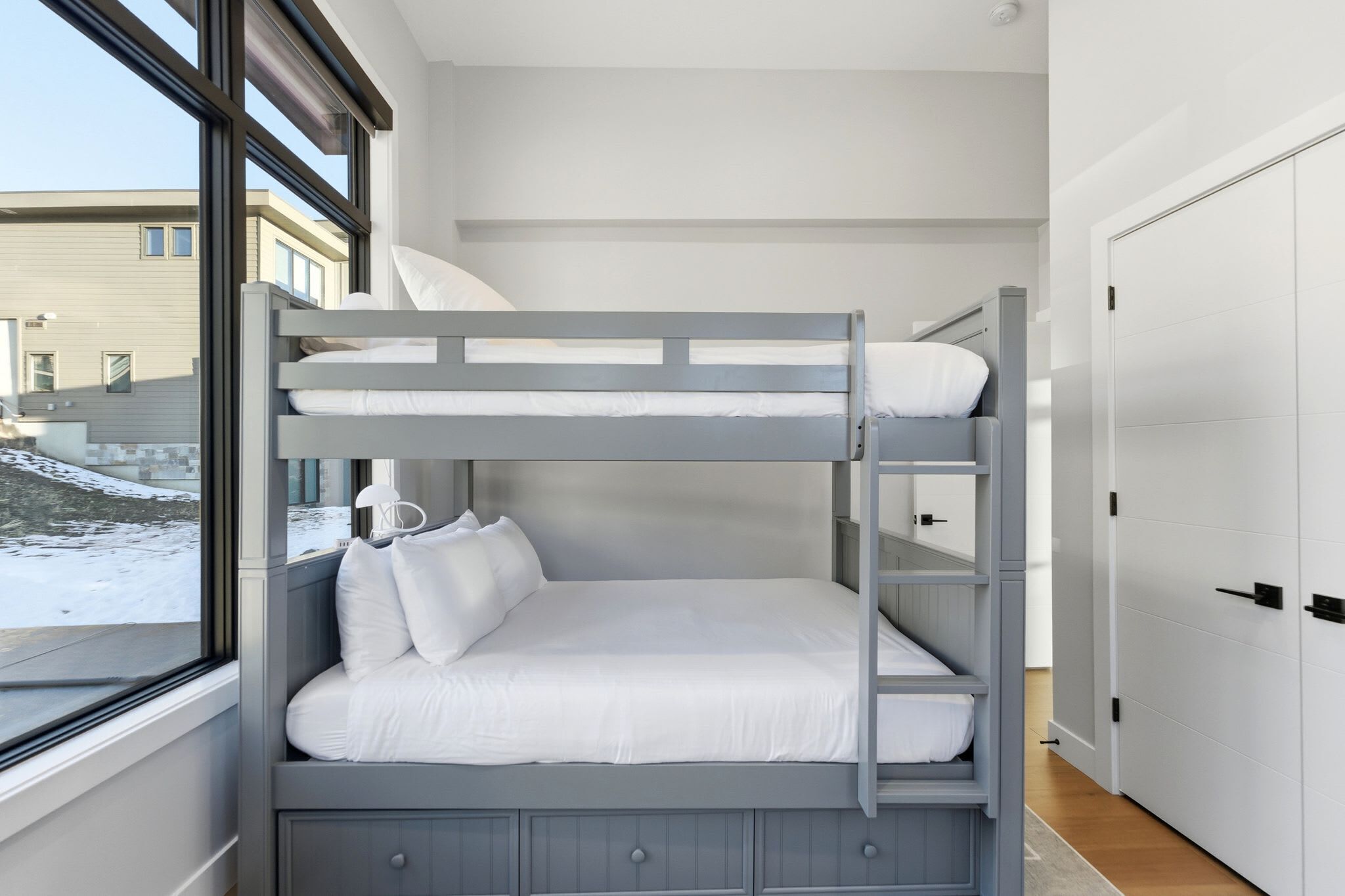A bunk bed room with a window view of a snowy landscape and a white door.
