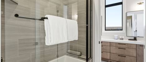 A modern bathroom with a glass-enclosed shower, a white bathtub, and a wooden vanity with a mirror.