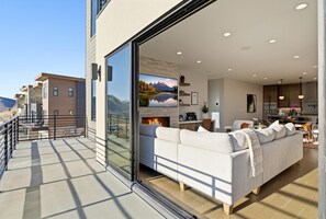 A modern living room with a large TV, a fireplace, and a balcony overlooking a mountainous landscape. - Upscale Retreat w/ Hot Tub, Steam, Pet-Friendly (Hideout)