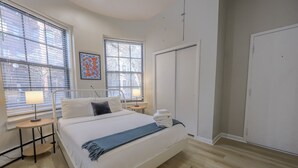 A bedroom with a bed, two bedside tables, a window, a door, and a wall-mounted artwork. - Stellar South End Studio (Boston)