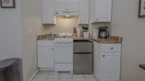 A compact kitchen with white cabinets, a gas stove, a built-in oven, a refrigerator, and a coffee maker. - Stellar South End Studio (Boston)