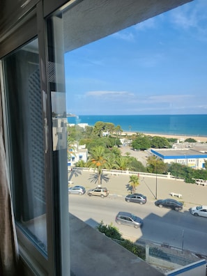 A view from a window overlooking a parking lot with several cars, a beach, and a clear sky. - Strategically located apartment close to all amenities (Marsa)