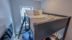 Ein gemütliches Schlafzimmer mit Etagenbett, einem kleinen Tisch mit Pflanze und einem Fenster mit Jalousien.