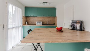 A modern kitchen with teal cabinets, a wooden countertop, a microwave, a coffee machine, and a red bowl. - Duplex apartment for 6 people (Arcachon)