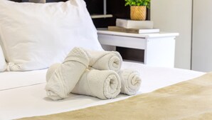 A neatly made bed with rolled white towels, a white pillow, and a small potted plant on a white nightstand. - Spacious studio apartment with balcony, air conditioning, garage, Wi-Fi, swimming pool, meeting rooms near Paulista Avenue. (São Paulo)