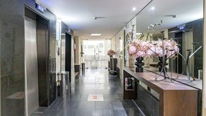 A modern hotel lobby with a reception desk, a large mirror, and an elevator. - Spacious studio apartment with balcony, air conditioning, garage, Wi-Fi, swimming pool, meeting rooms near Paulista Avenue. (São Paulo)
