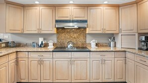Eine moderne Küche mit hellen Holzschränken, Granitwerkplatten, einer Edelstahl-Dunstabzugshaube und einer integrierten Mikrowelle.