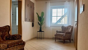 Une pièce comprenant un canapé à motifs, un fauteuil, une plante en pot, une décoration murale en bois et une fenêtre donnant sur un paysage.