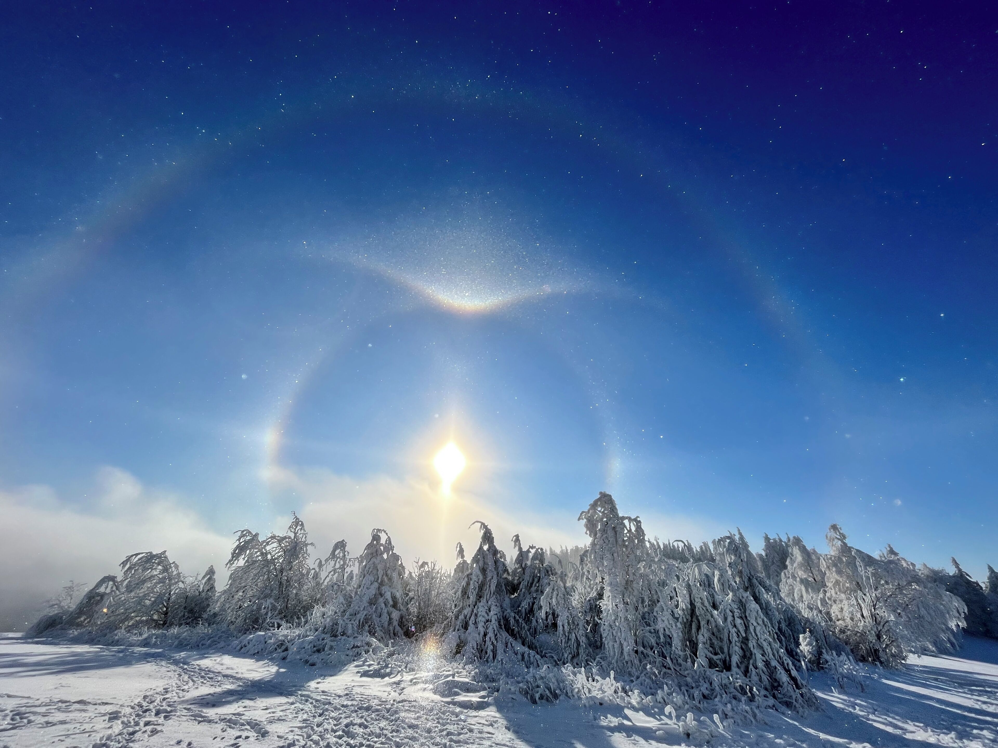 Un paysage enneigé, avec un ciel dégagé et un soleil visible.