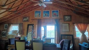 A rustic wooden interior with a high ceiling, a ceiling fan, and a dining area with chairs and a table.