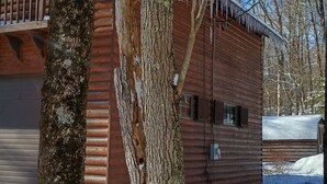 A wooden cabin with a garage, surrounded by snow and trees.