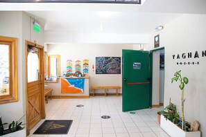 Un espace d’accueil avec un bureau en bois, un banc, une porte verte et un mur sur lequel est affiché un panneau indiquant « YAGHAN ».