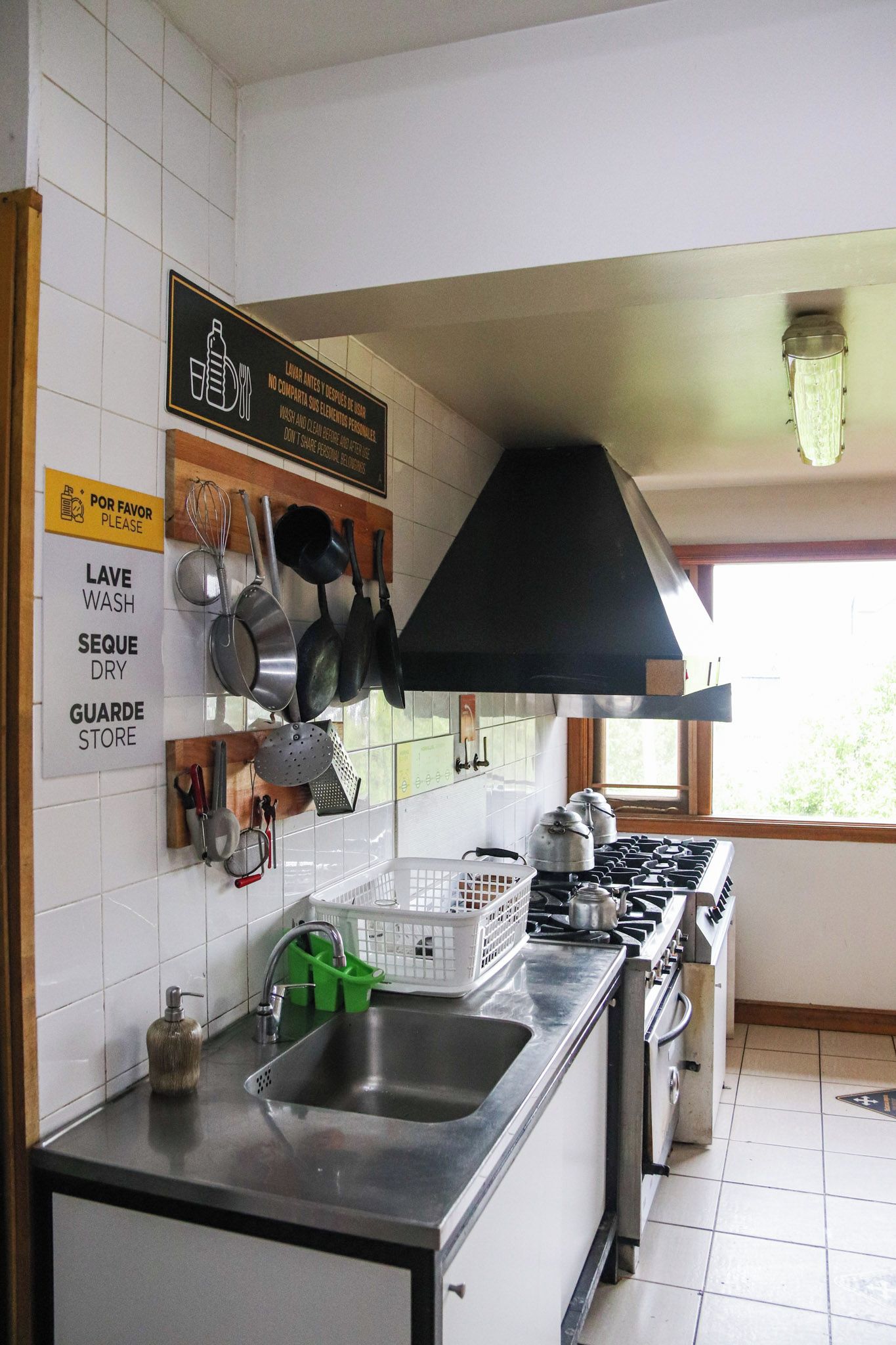 Una cocina con estufa, lavaplatos y varios utensilios colgados en la pared. Hay letreros que indican lavar y secar los platos.