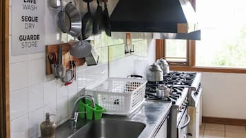 Una cocina con estufa, lavaplatos y varios utensilios colgados en la pared. Hay letreros que indican lavar y secar los platos.