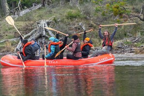 Un groupe de personnes se trouve dans un canot pneumatique rouge sur lequel on peut lire les mots « Lakes » et « Isla ». Elles pagayent sur une rivière paisible.