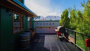 A deck with wooden barrels, a barbecue grill, and a sign reading "YAGHAN". - YAGHAN HOSTEL (Ushuaia)
