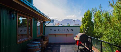A deck with wooden barrels, a barbecue grill, and a sign reading "YAGHAN".
