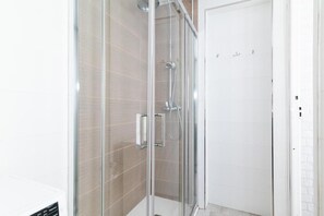 Eine gläserne Duschkabine mit Bedienfeld, beige geflieste Wände und einer weißen Tür.