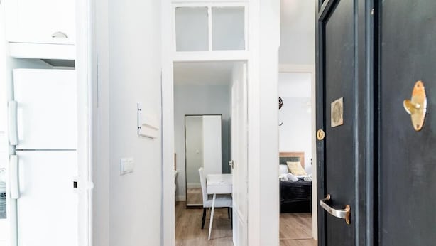 Ein Flur mit einer weißen Tür, die zu einem Zimmer mit Bett und Schreibtisch führt.