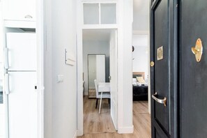 Un pasillo con una puerta blanca que da a una habitación con una cama y un escritorio.