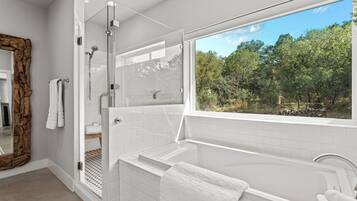 A modern bathroom with a glass-enclosed shower, a large bathtub, and a view of the outdoors.