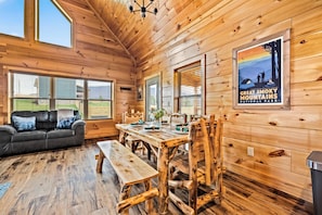 A wooden cabin interior with a dining table, benches, a sofa, and a poster of the Great Smoky Mountains National Park. - Misty Morning Cabin, sit back & relax with beautiful mountain views! Pups Yes! (Cosby)