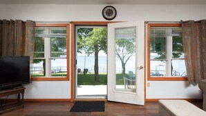 Una sala de estar con televisor, un banco y una puerta que da a un balcón con vistas al mar.