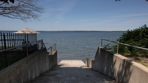 Una escalera de hormigón conduce a un muelle a orillas de aguas tranquilas, con una barandilla de metal en un lado y un muro de hormigón en el otro.