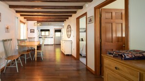 Una habitación amplia con suelo de madera, un comedor con mesa y sillas, una cama con colcha y una puerta de madera.
