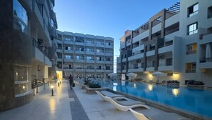 Un immeuble résidentiel moderne doté d’une piscine, d’un espace extérieur aménagé et d’un chemin piétonnier bien éclairé.