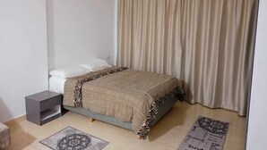 Une chambre à coucher avec un lit, une table de chevet, une lampe suspendue et un rideau.