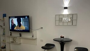 Un salon avec un téléviseur fixé au mur, une enseigne portant l’inscription « FAMILLE » et trois tabourets de bar noirs.