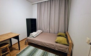 Ein kleines, ordentlich eingerichtetes Schlafzimmer mit einem Einzelbett, einem Holztisch und einem Stuhl.