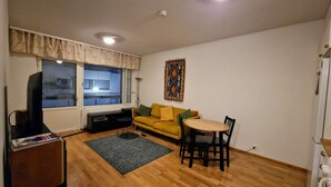 Ein Wohnzimmer mit einer Couch, einem kleinen runden Tisch, einem Fernseher und einem Fenster mit Jalousien.