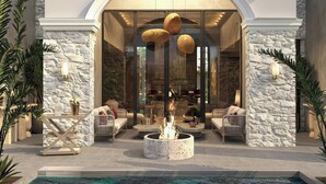 Una zona relax esterna moderna con pareti in pietra, sedute confortevoli, un elemento centrale a forma di focolare e una piscina.