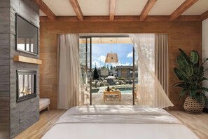 Un dormitorio con una cama grande, vigas de madera, pared de piedra, una ventana y vista a una piscina y zona exterior.