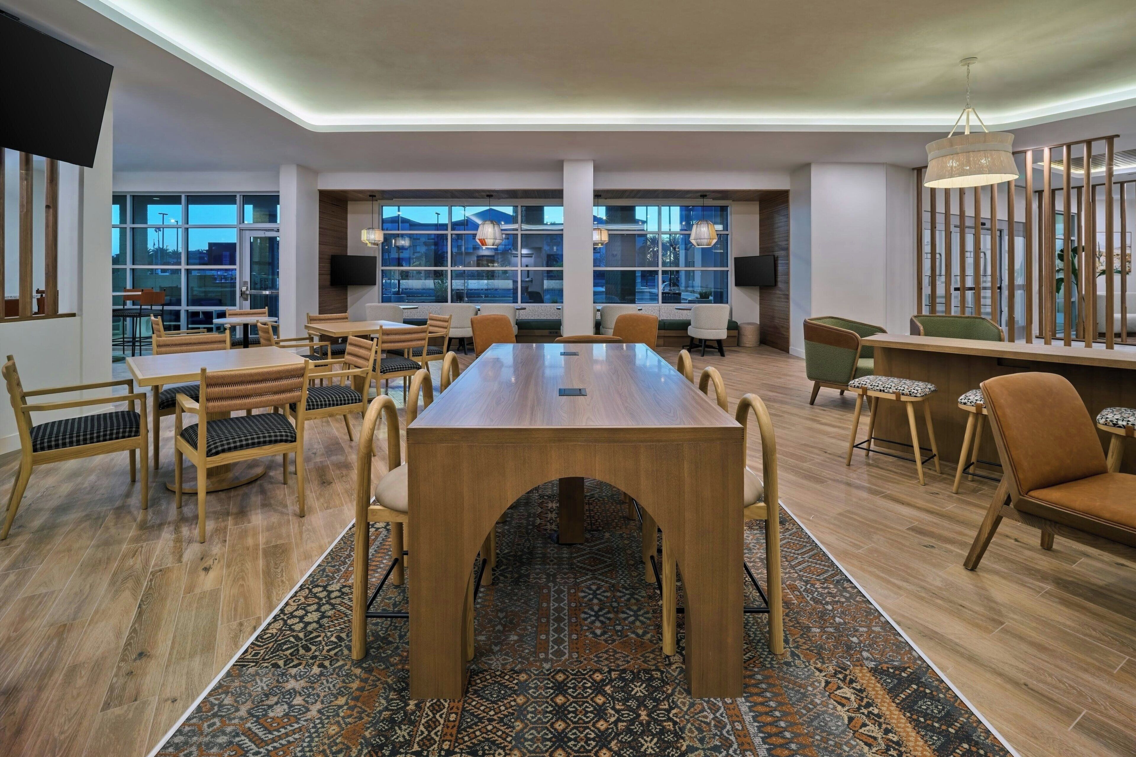 Uma sala de reuniões ampla com uma grande mesa de madeira, várias cadeiras e um tapete estampado.