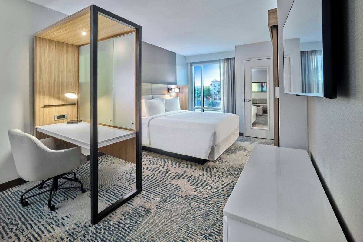 A hotel room with a bed, desk, chair, and a large mirror.